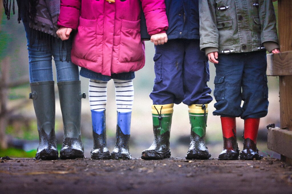 Vier kinderen in modderige laarzen. Alleen de benen gefotografeerd.